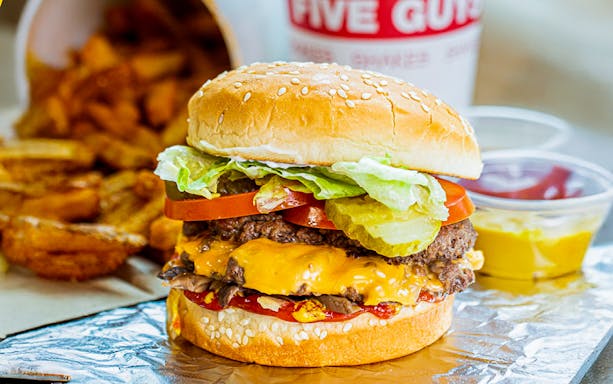 Burger with cheese, lettuce, tomato, and pickles, served with fries at Five Guys, Dubai Marina.