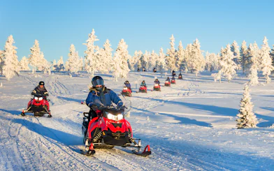 Snowmobilers riding across a snowy landscape in Lapland during winter.