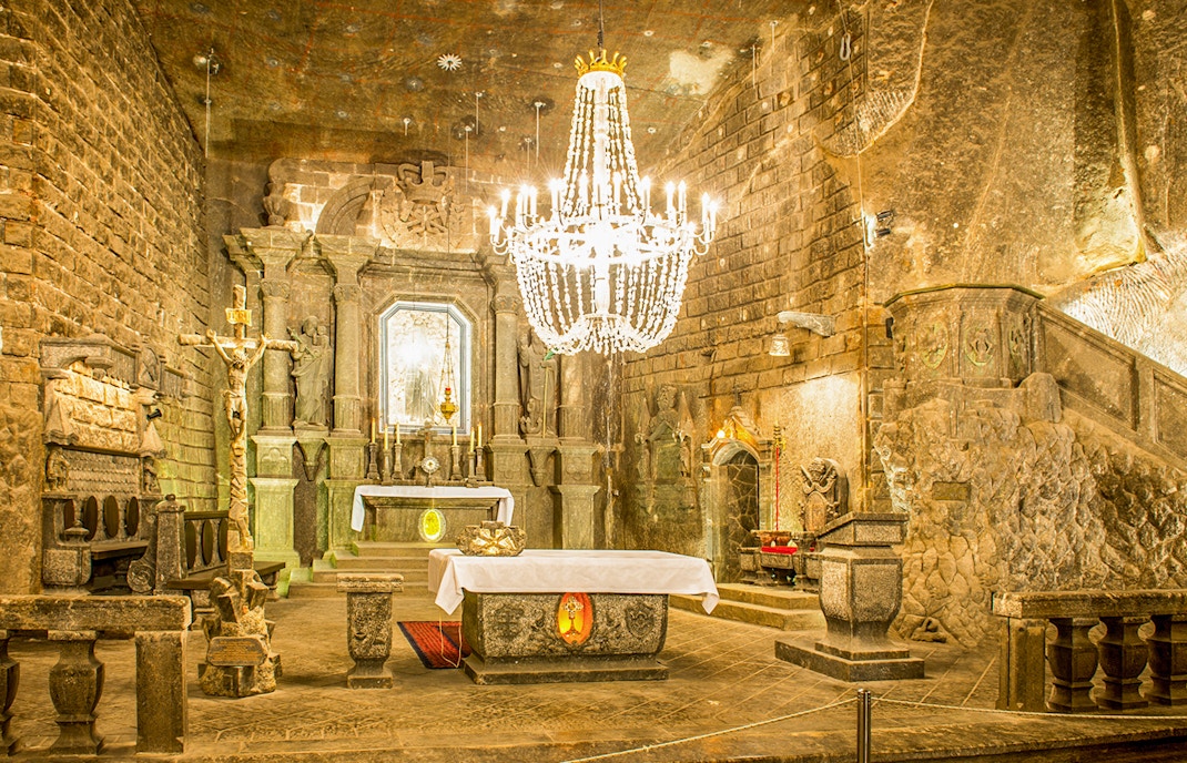 Hell erleuchtete Kapelle mit dreiteiligem Alter, Kreuz und Kronleuchter im Salzbergwerk Wieliczka