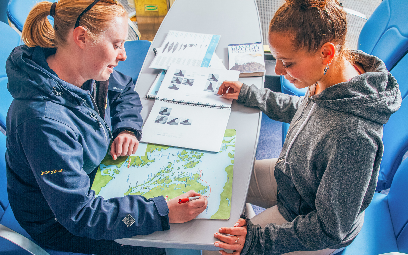 Two women planning a route on a map at a table with travel guides.