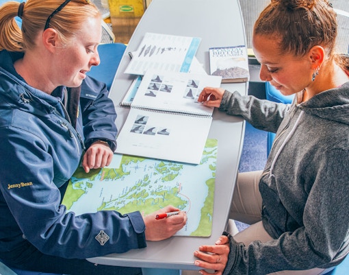 Two women planning a route on a map at a table with travel guides.