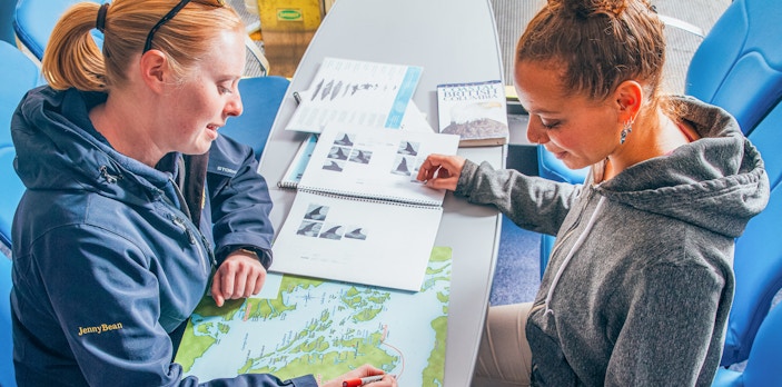 Two women planning a route on a map at a table with travel guides.