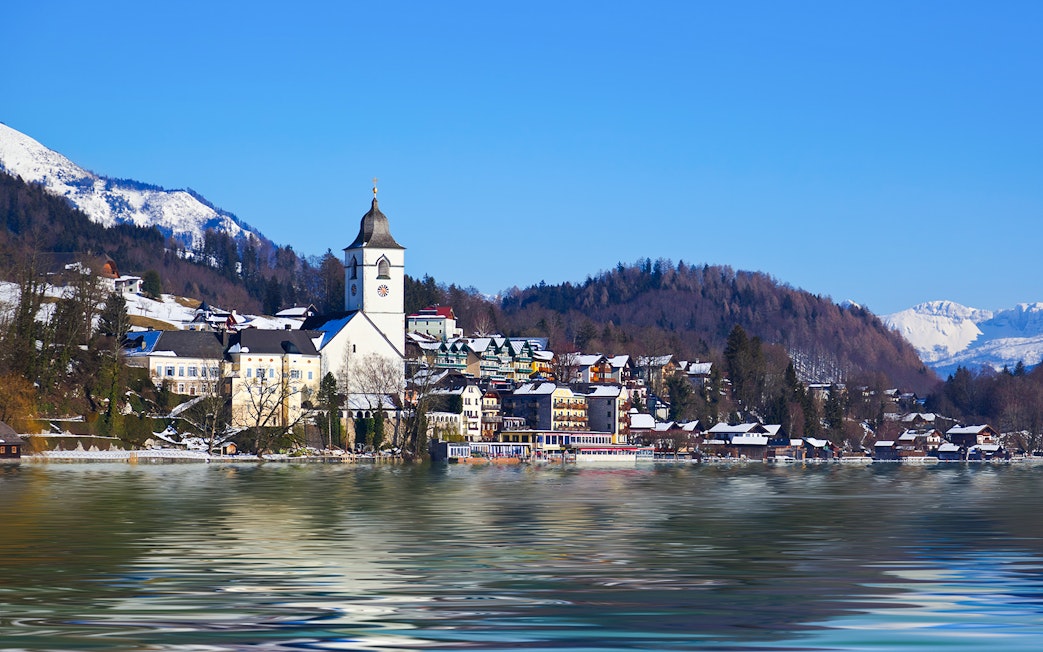 Church and village by Lake Wolfgangsee, Salzburg, Austria, with snow-covered mountains in winter.