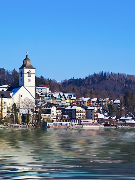 Church and village by Lake Wolfgangsee, Salzburg, Austria, with snow-covered mountains in winter.