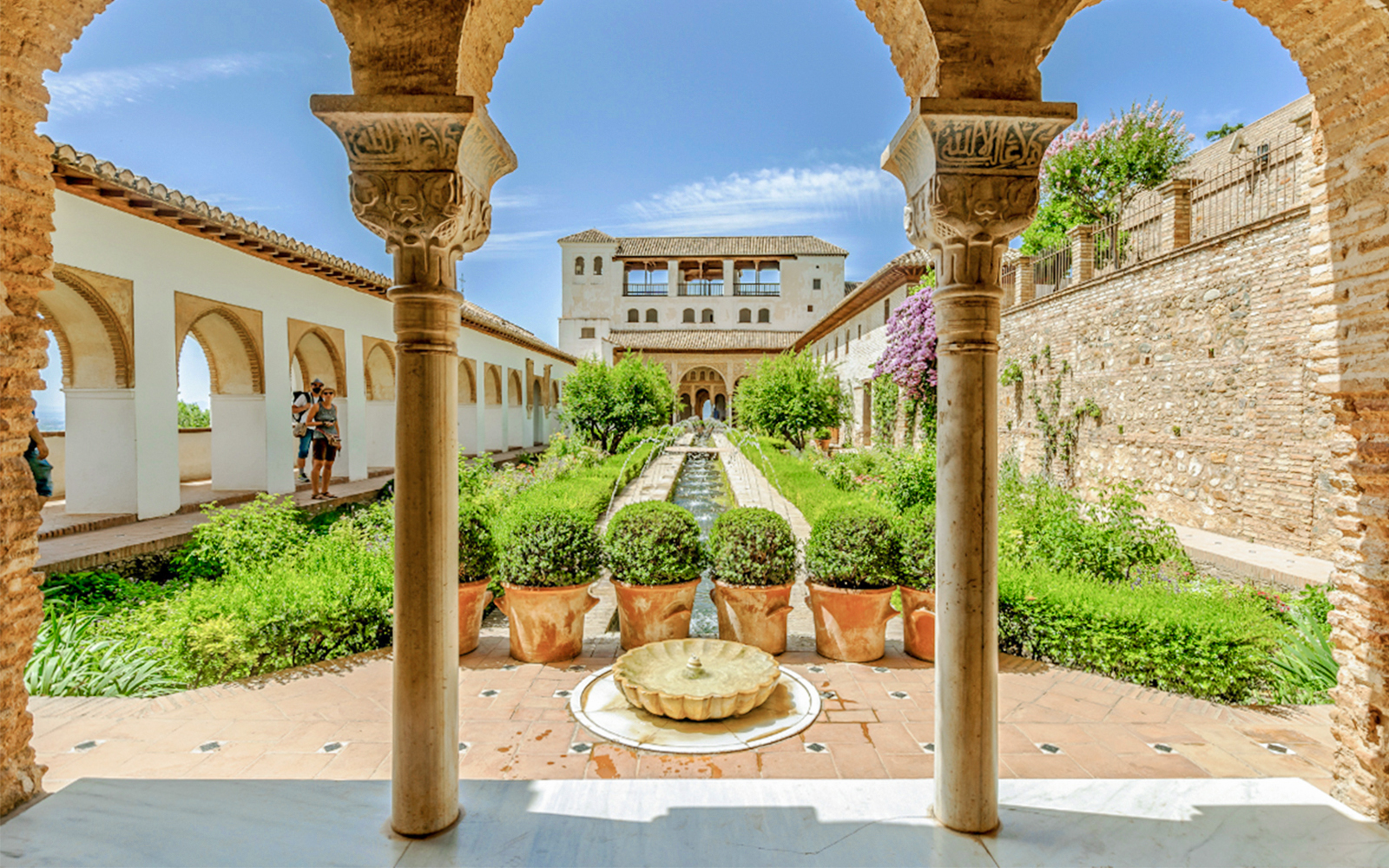 Courtyard view of Alhambra's Nasrid Palaces with arches, gardens, and central fountain in Granada, Spain.