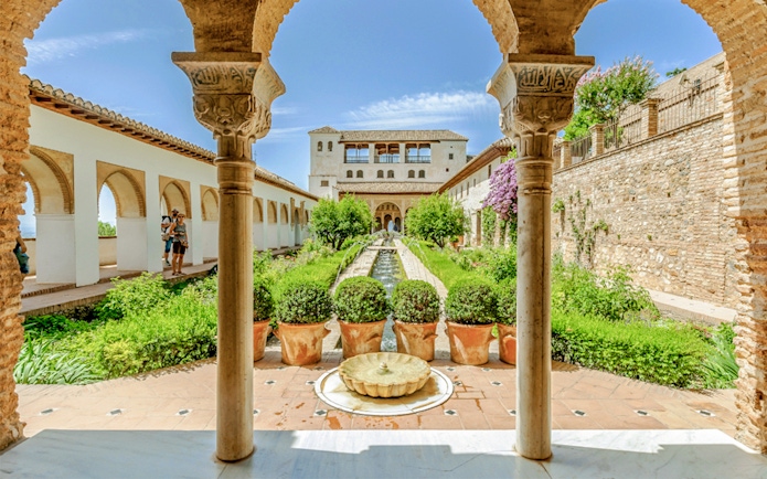 Courtyard view of Alhambra's Nasrid Palaces with arches, gardens, and central fountain in Granada, Spain.