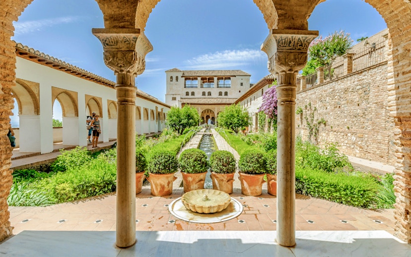 Courtyard view of Alhambra's Nasrid Palaces with arches, gardens, and central fountain in Granada, Spain.