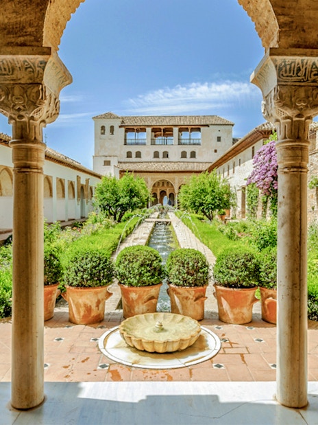 Courtyard view of Alhambra's Nasrid Palaces with arches, gardens, and central fountain in Granada, Spain.