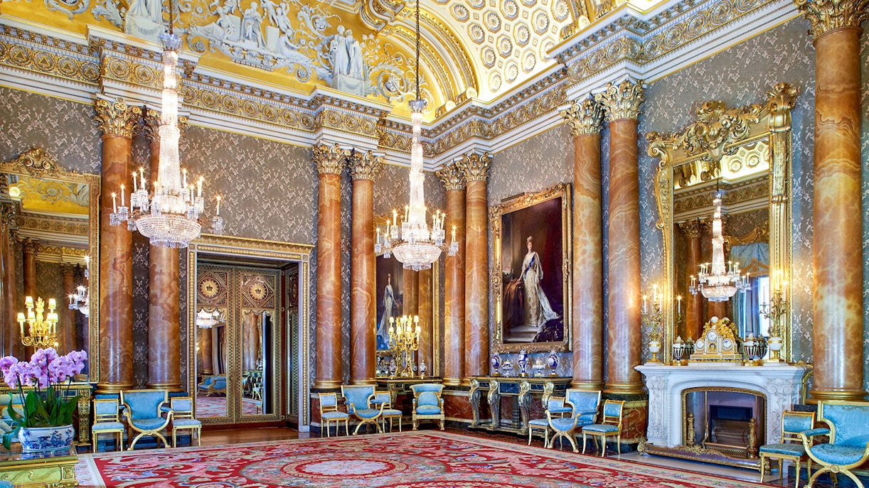 Blue Drawing Room at Buckingham Palace with chandeliers, ornate columns, and regal portraits.