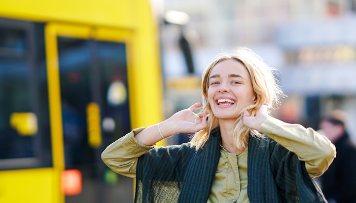 Woman smiling in front of a yellow tram.