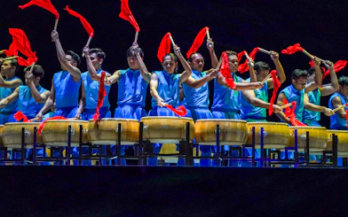 Performers in blue costumes playing drums with red flags at Encore Melaka show.