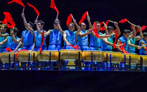 Performers in blue costumes playing drums with red flags at Encore Melaka show.