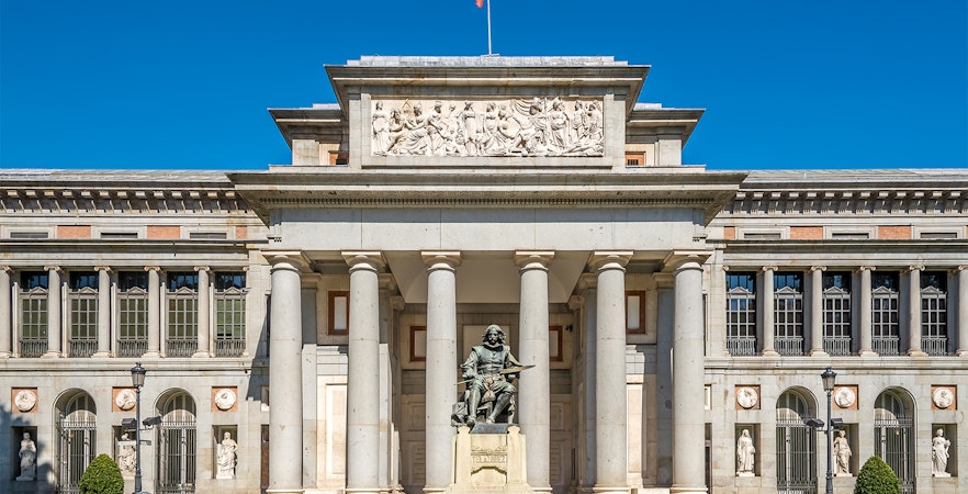 Prado Museum entrance in Madrid with visitors and a HOHO bus in the background.