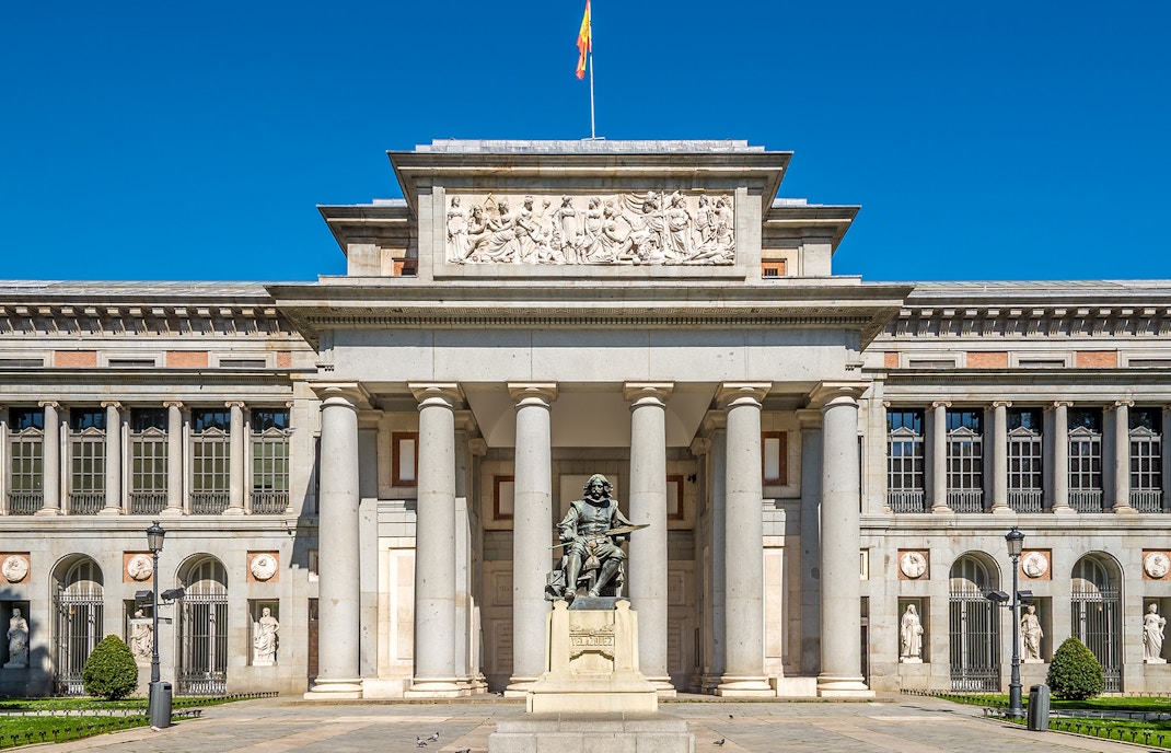 Prado Museum entrance in Madrid with visitors and HOHO bus in the background.