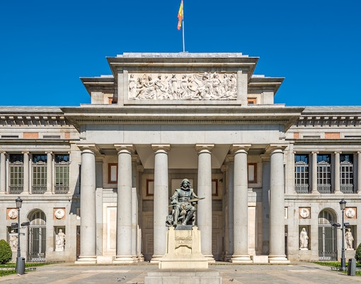 Prado Museum entrance in Madrid with visitors and a HOHO bus in the background.