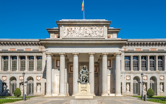 Prado Museum entrance in Madrid with visitors and a HOHO bus in the background.