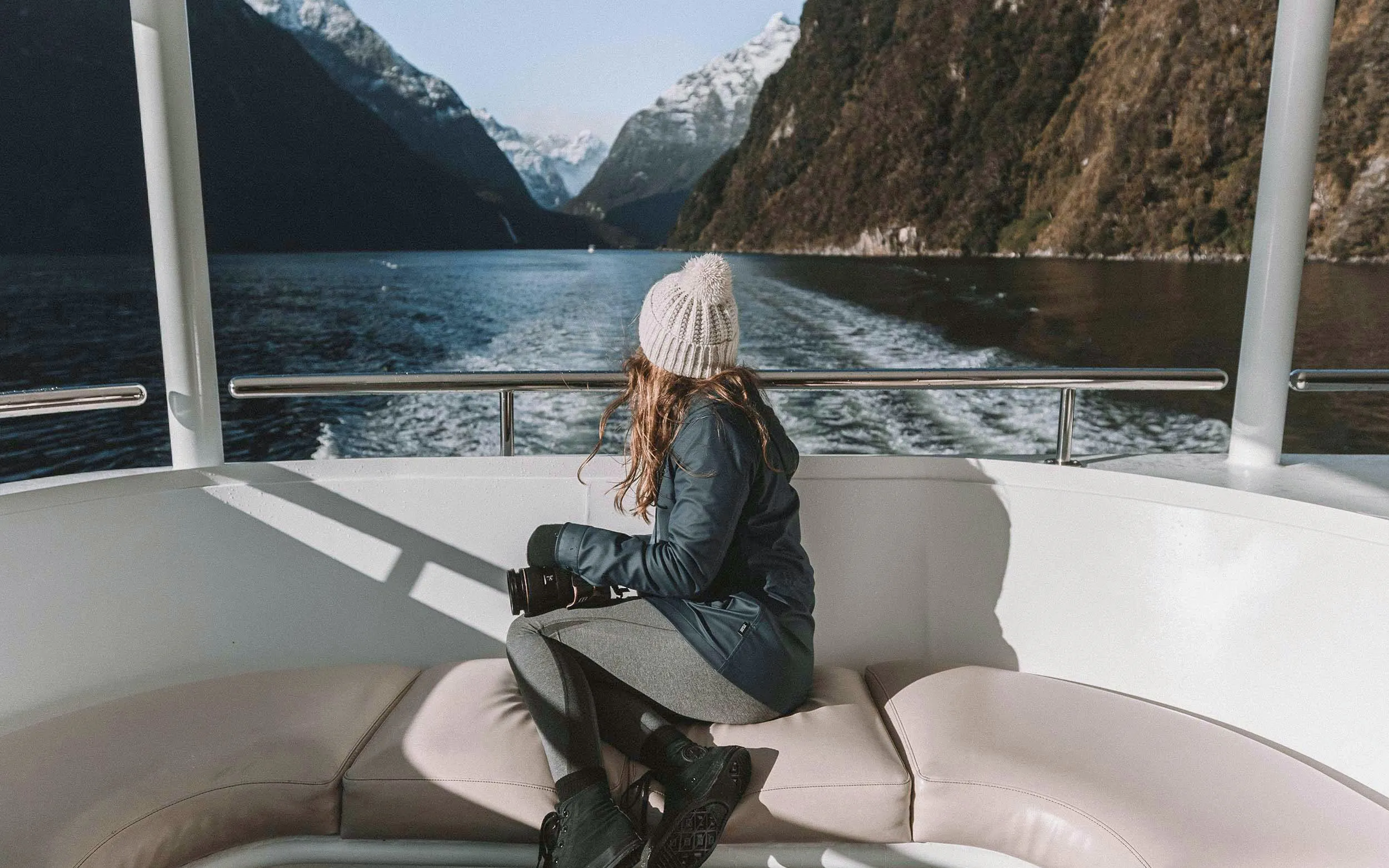Person on a boat enjoying views of Milford Sound fjord, New Zealand, with snow-capped mountains.