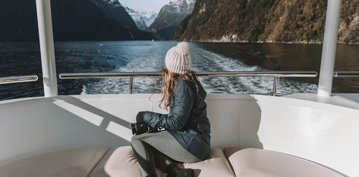 Person on a boat enjoying views of Milford Sound fjord, New Zealand, with snow-capped mountains.