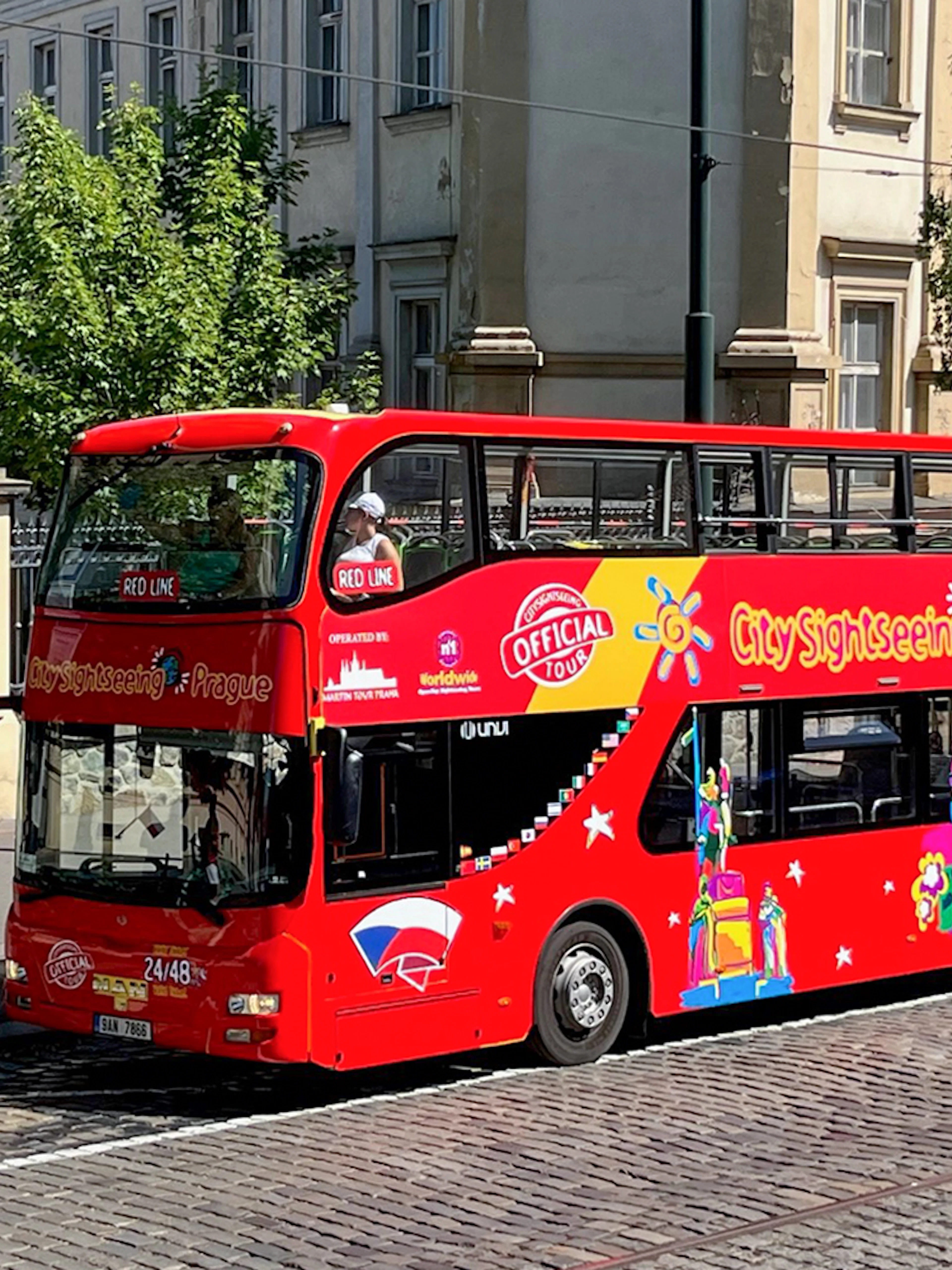 Red double-decker bus for City Sightseeing Prague Hop-On Hop-Off Tour on a cobblestone street.