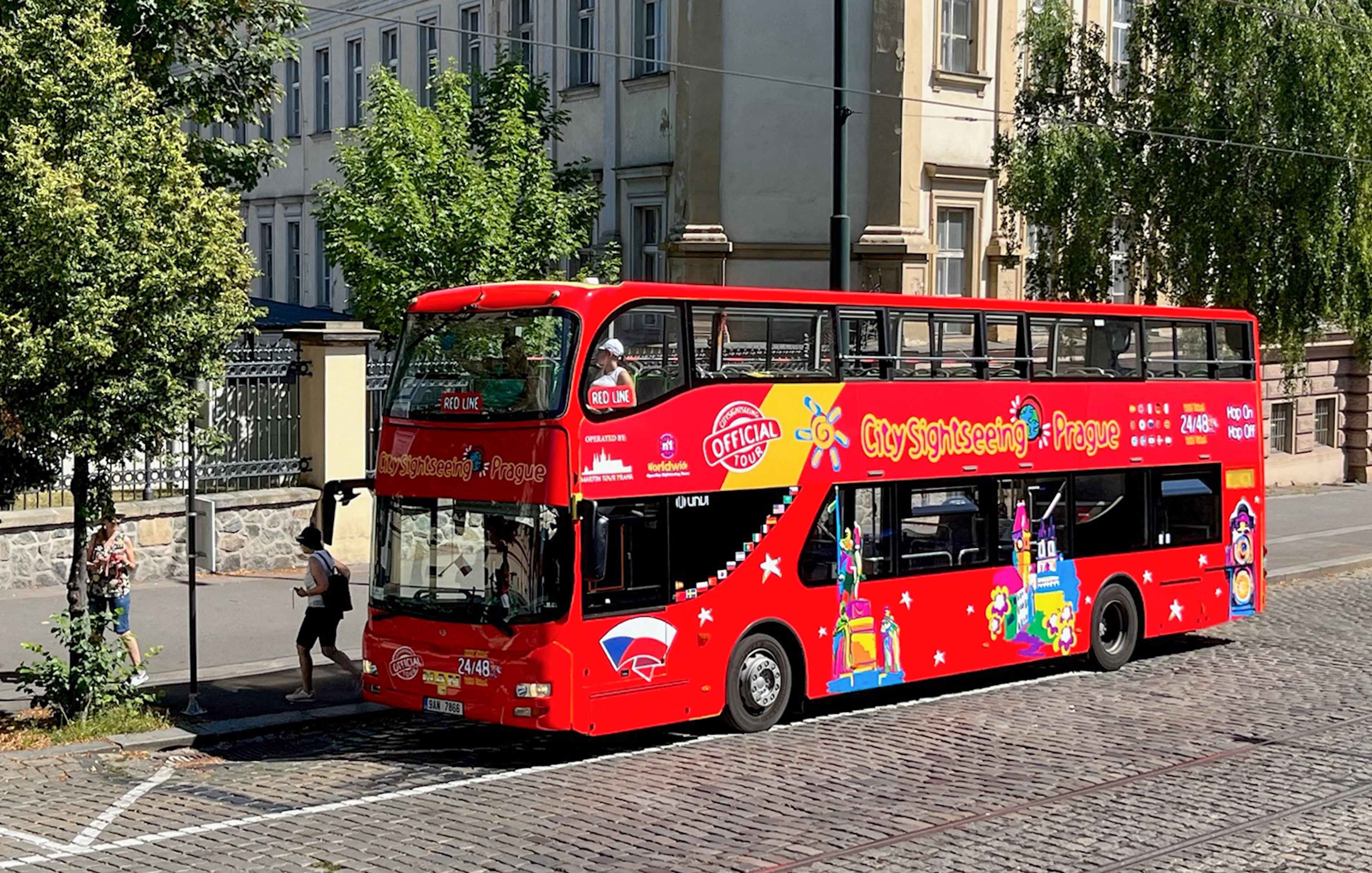 Red double-decker bus for City Sightseeing Prague Hop-On Hop-Off Tour on a cobblestone street.