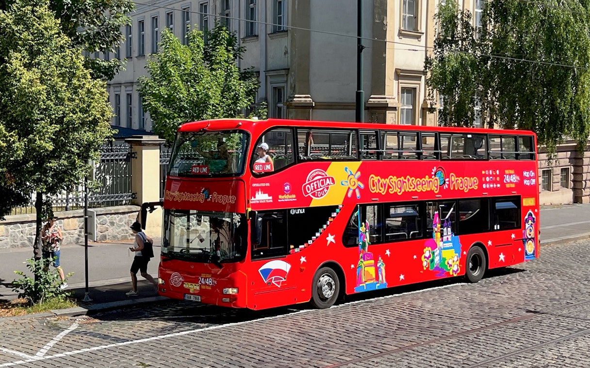Red double-decker bus for City Sightseeing Prague Hop-On Hop-Off Tour on a cobblestone street.