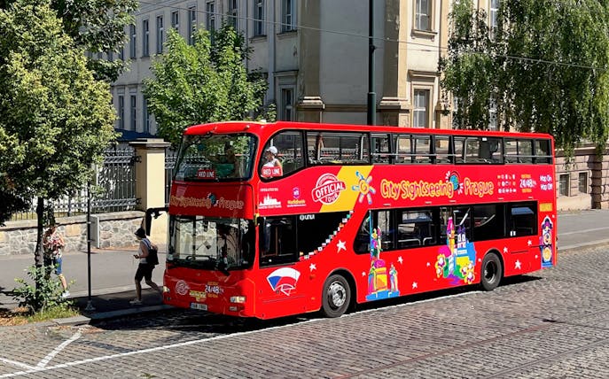 Red double-decker bus for City Sightseeing Prague Hop-On Hop-Off Tour on a cobblestone street.