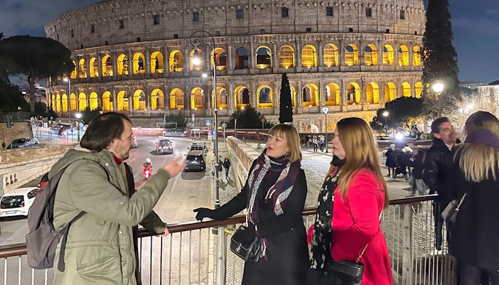 Walking tour group at the illuminated Colosseum in Rome at night.