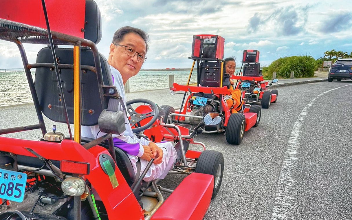 People driving red go-karts along a coastal road in Okinawa.
