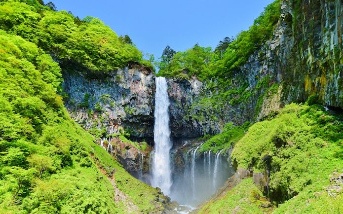 Kegon Falls cascading down a rocky cliff surrounded by lush greenery in Nikko, Japan.