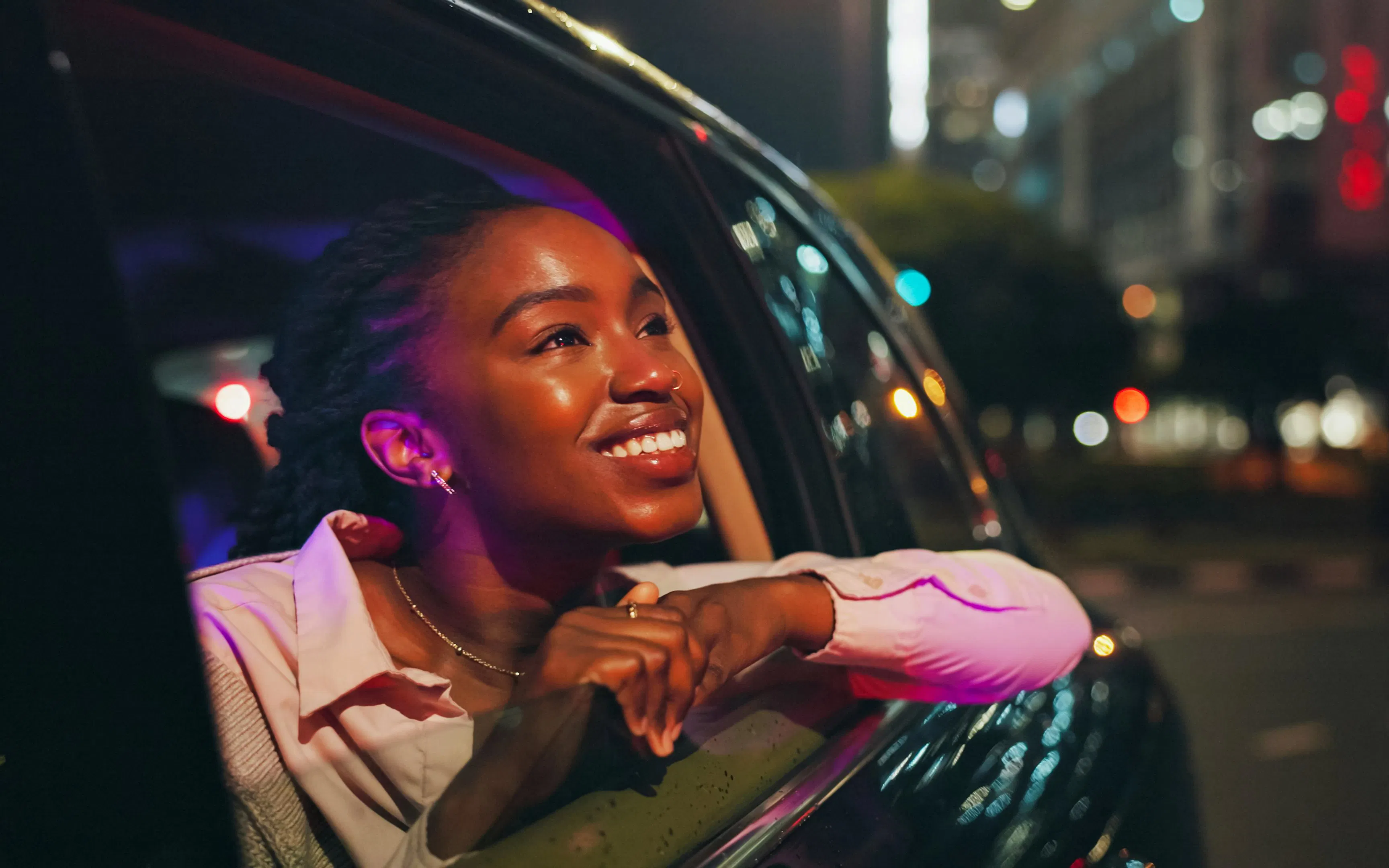 Woman looking out car window at city lights at night.