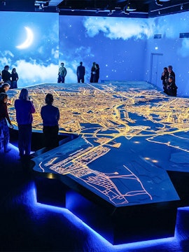 Visitors observing illuminated Amsterdam city map at the Amsterdam in Motion exhibit.