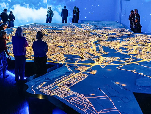 Visitors observing illuminated Amsterdam city map at the Amsterdam in Motion exhibit.