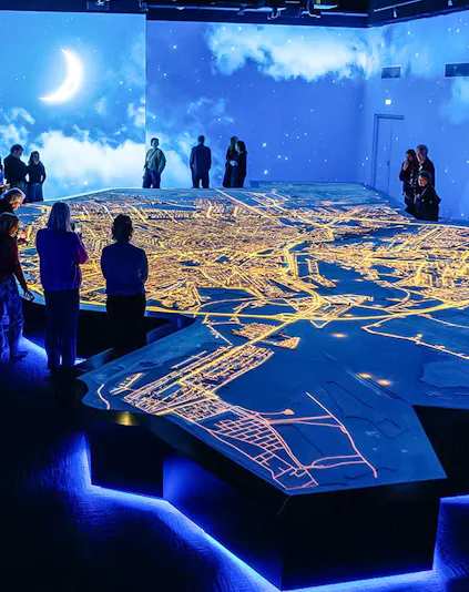 Visitors observing illuminated Amsterdam city map at the Amsterdam in Motion exhibit.
