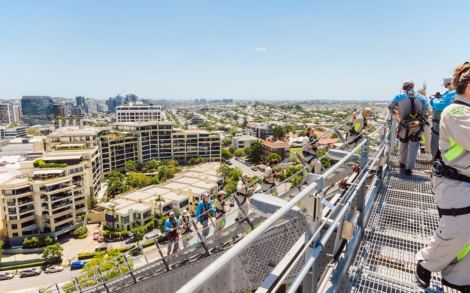 Climbers in harnesses on Story Bridge arch with view of Brisbane cityscape.