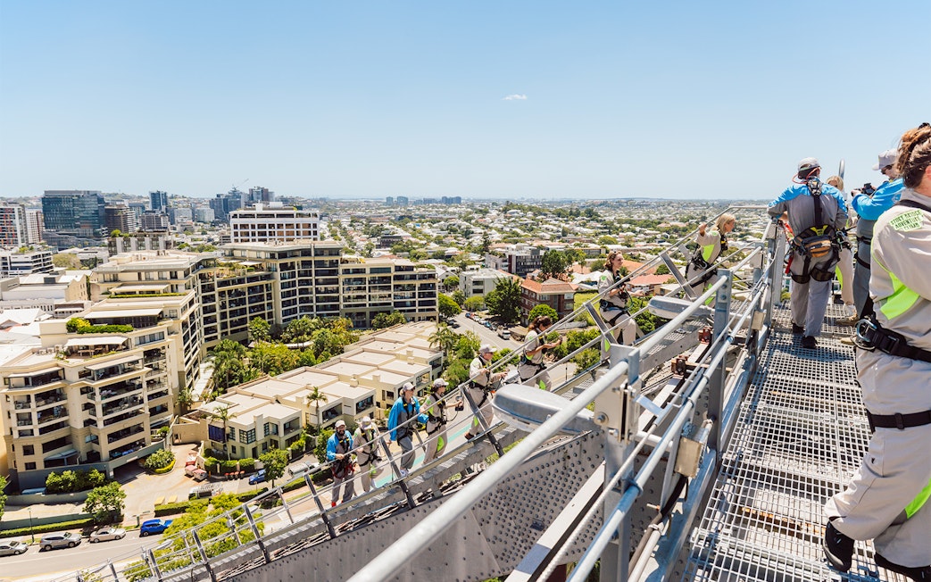 Climbers in harnesses on Story Bridge arch with view of Brisbane cityscape.