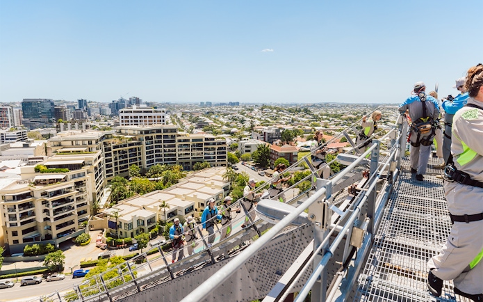 Climbers in harnesses on Story Bridge arch with view of Brisbane cityscape.