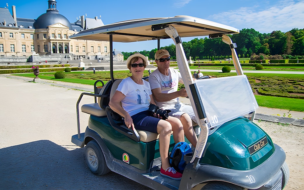Visitors in a golf cart at Vaux-le-Vicomte, France, with the château in the background.