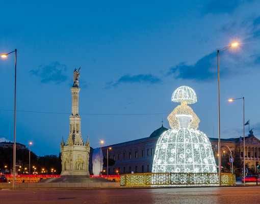 Illuminated Menina sculpture at night near a monument in Madrid, Spain during Christmas.