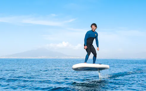 Person e-foiling on the sea near Capri with distant mountains in the background.