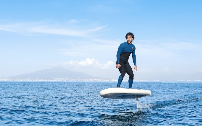 Person e-foiling on the sea near Capri with distant mountains in the background.