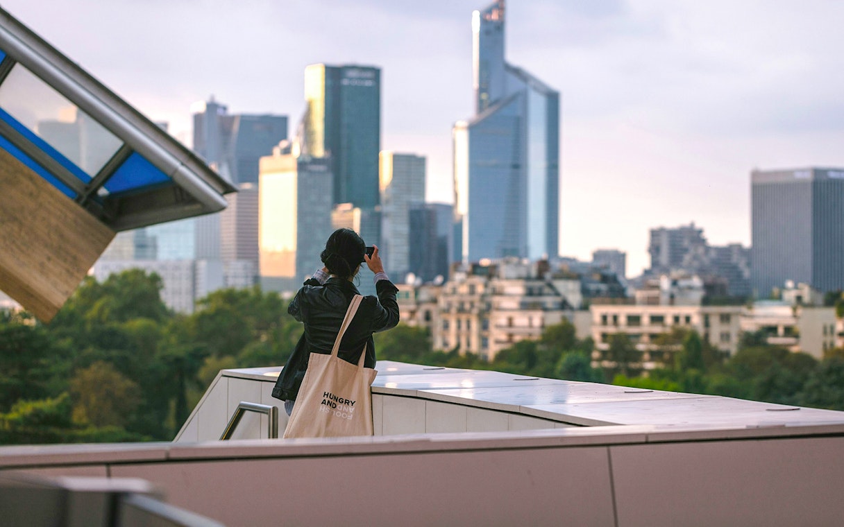 Woman photographing Paris skyline from Fondation Louis Vuitton rooftop.