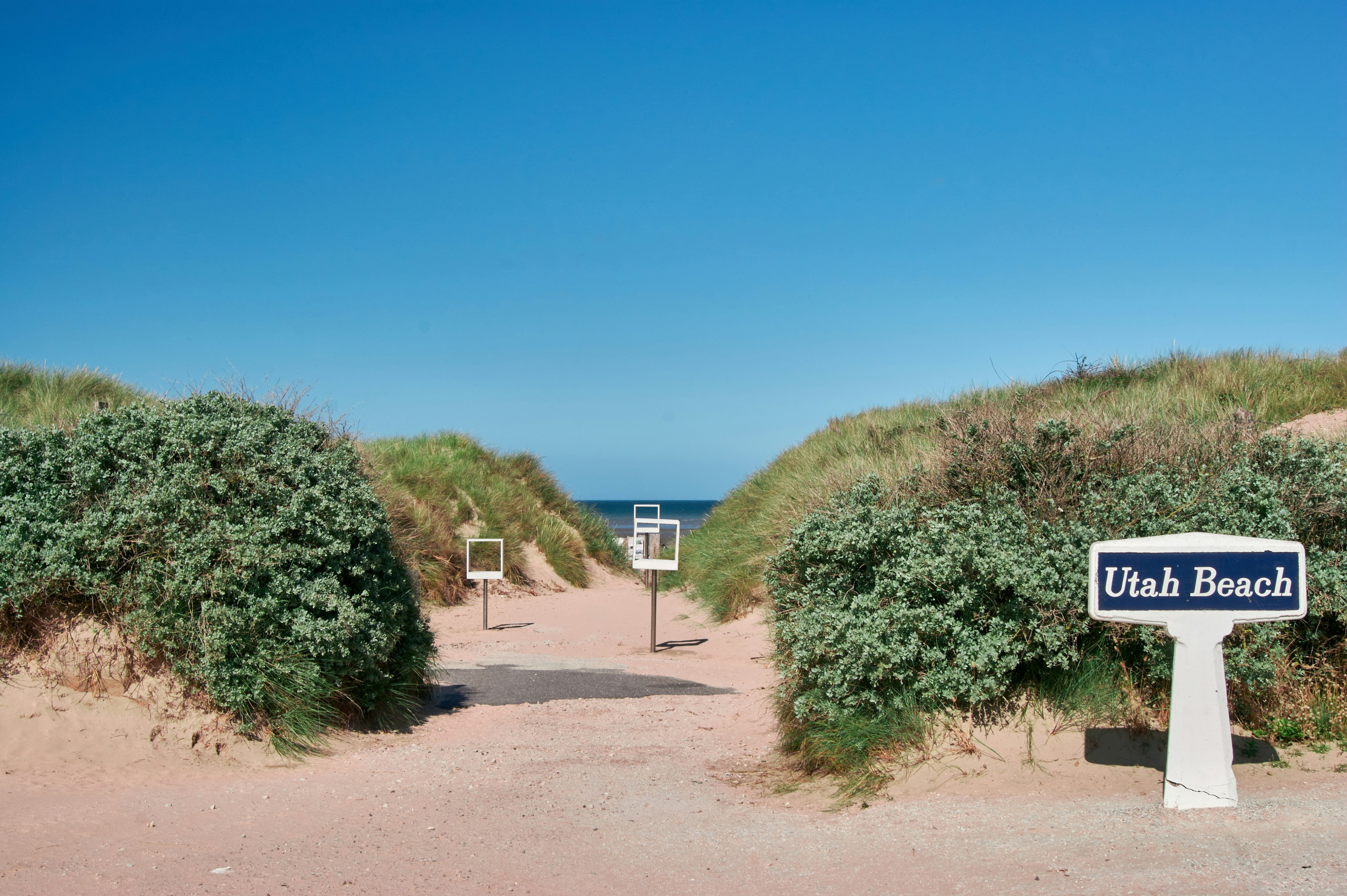 Pathway through sand dunes leading to Utah Beach, Normandy, with a sign marking the location.