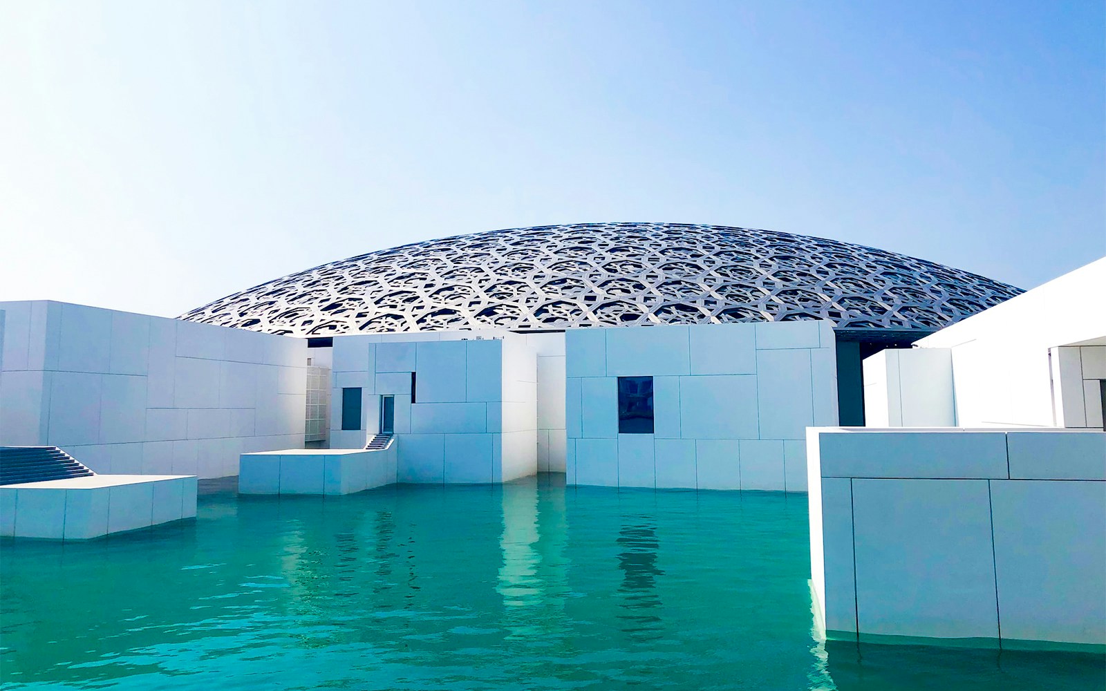 Louvre Abu Dhabi exterior with geometric dome and water reflection.