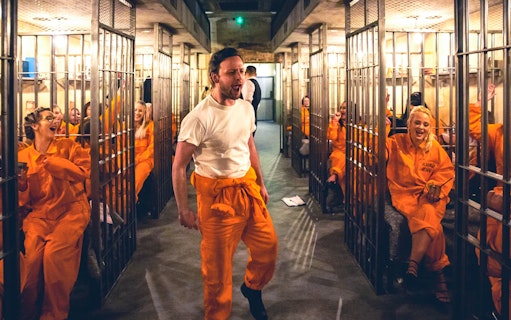 Guests in orange jumpsuits enjoying Alcotraz prison-themed cocktail bar experience.