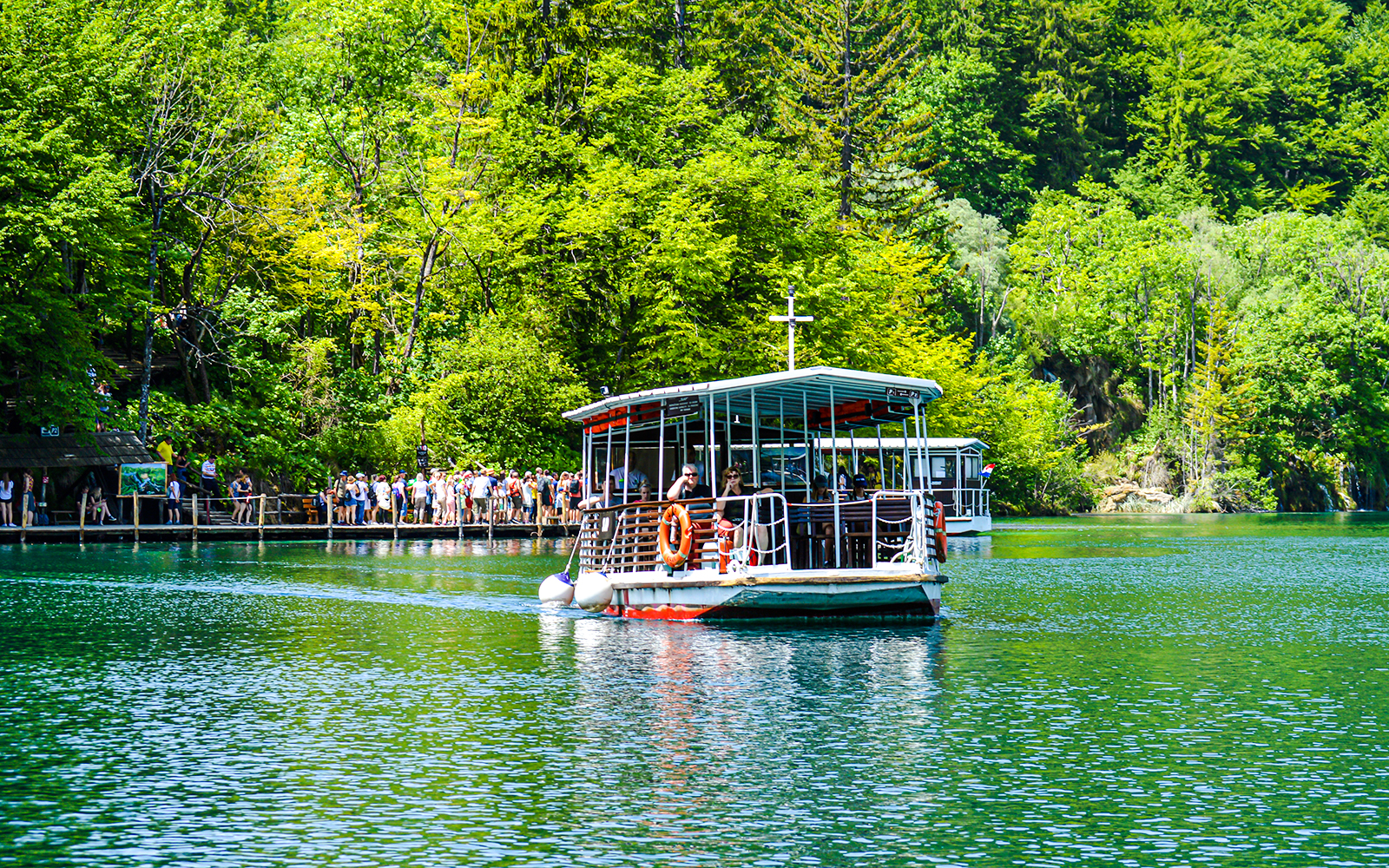 Boat with guests on Plitvice Lakes, Croatia, surrounded by lush greenery.