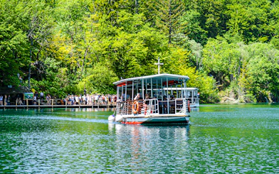 Boat with guests on Plitvice Lakes, Croatia, surrounded by lush greenery.