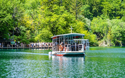 Boat with guests on Plitvice Lakes, Croatia, surrounded by lush greenery.