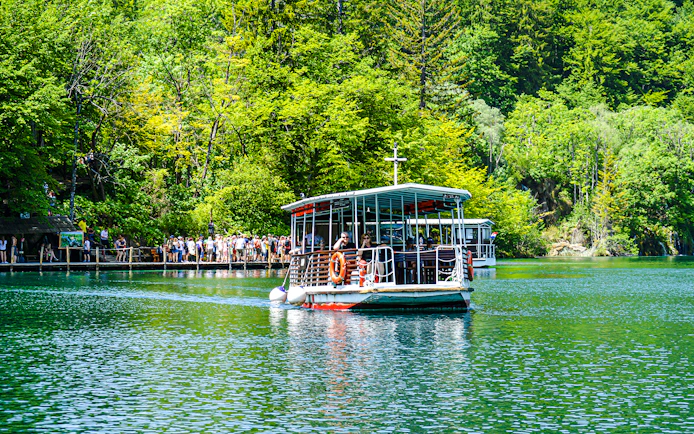 Boat with guests on Plitvice Lakes, Croatia, surrounded by lush greenery.