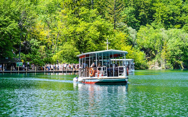 Boat with guests on Plitvice Lakes, Croatia, surrounded by lush greenery.