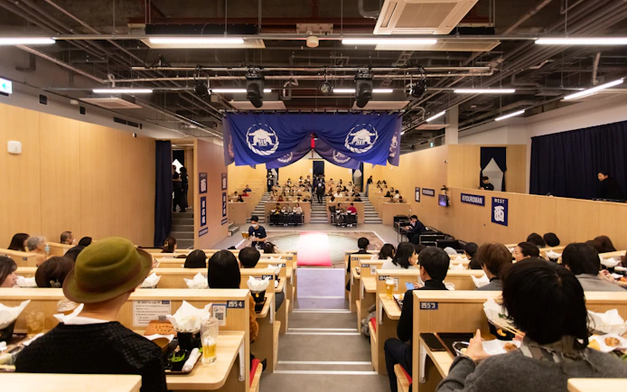 Kyoto sumo show audience dining on chicken hot pot in theater setting.